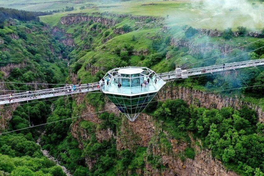 A glass-bottomed viewing platform with people on a suspension bridge over a canyon. 4