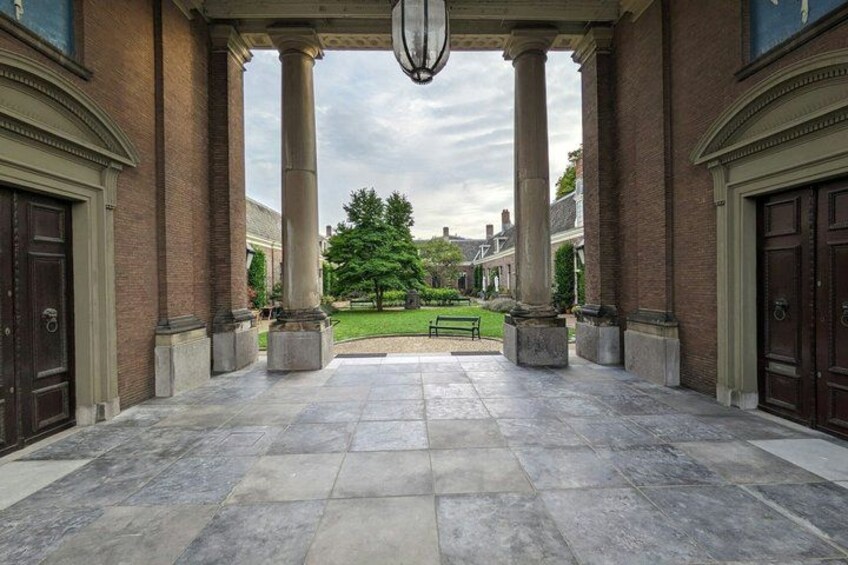 A building entrance with a stone floor, large columns, and a tree in the background. 1