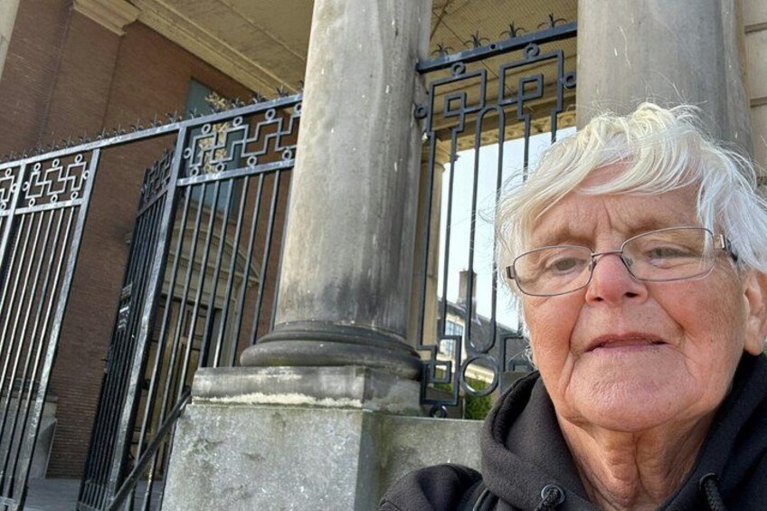 An elderly person standing in front of a building with a metal gate and columns. 4