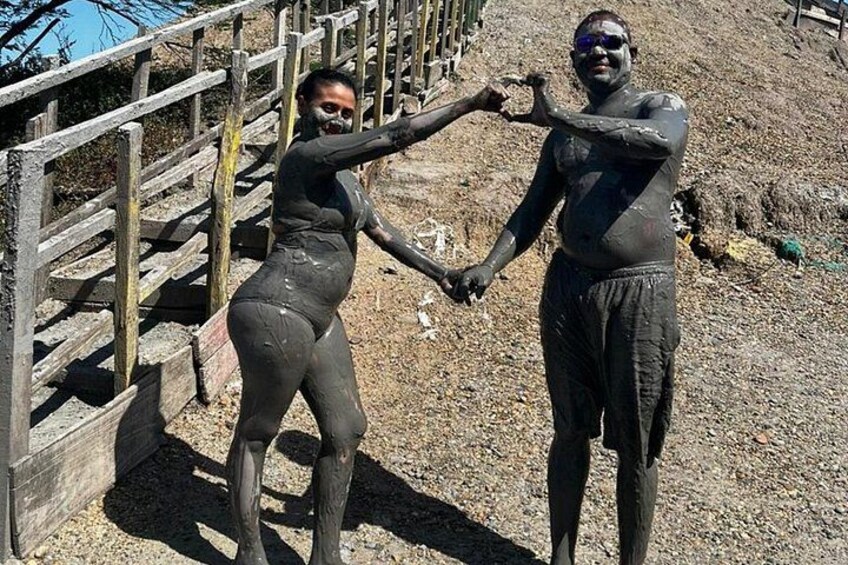 Two people in mud, holding hands, with a wooden fence and a gravel path in the background. 1