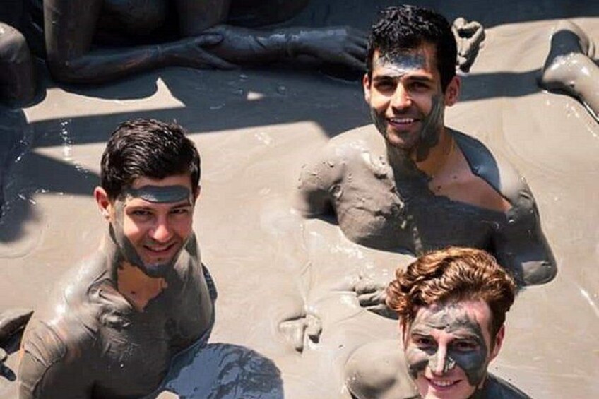 Three people covered in mud, sitting in a shallow water body. 5