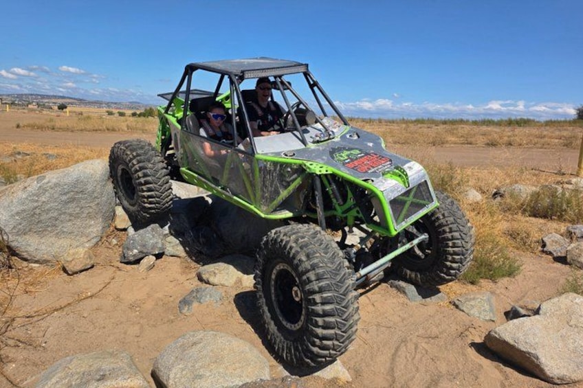 A green off-road vehicle on a rocky terrain with a clear sky. 3