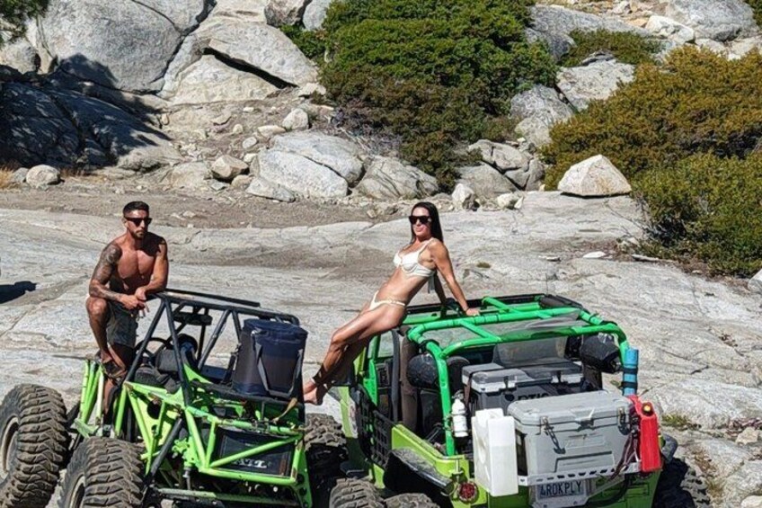 Two people on a green off-road vehicle with a rocky landscape in the background. 4
