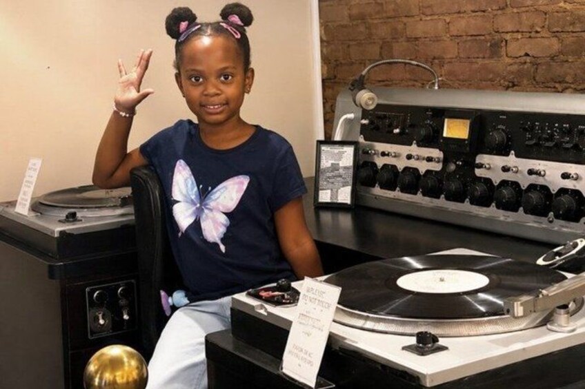 A person sitting at a turntable with a butterfly t-shirt, a brick wall in the background, and a vintage audio mixer. 4