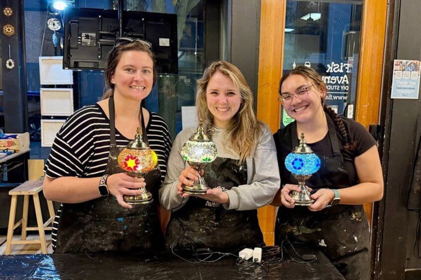 Three individuals holding decorative items in a workshop setting. 1