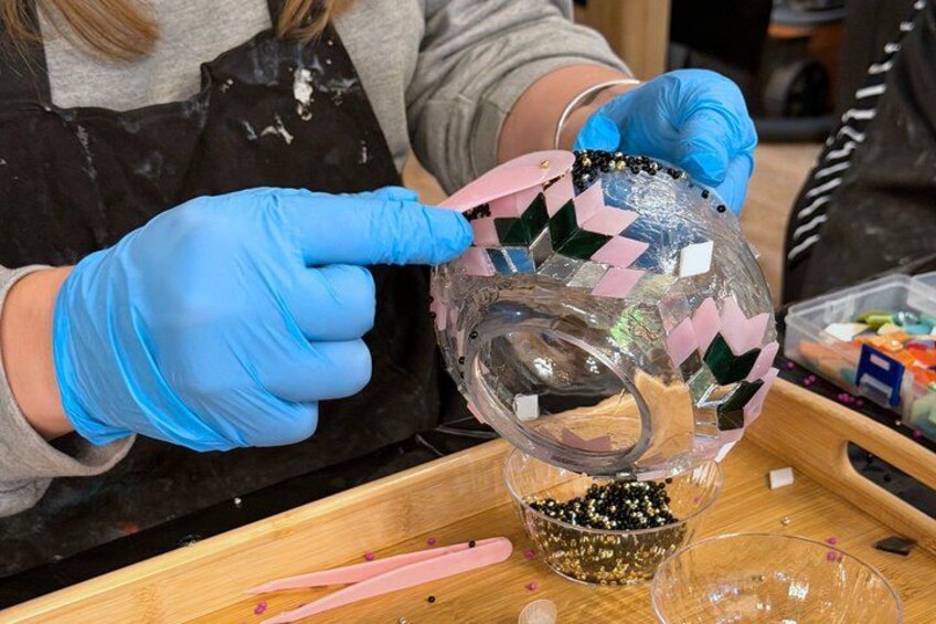 A person wearing blue gloves handling a clear glass object with colorful tape. 5