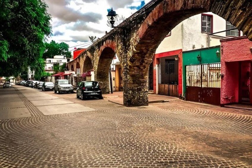 A cobblestone street under a stone bridge with parked cars and buildings on either side. 4