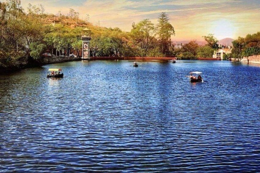 A calm lake with boats, a tower, and trees. 1