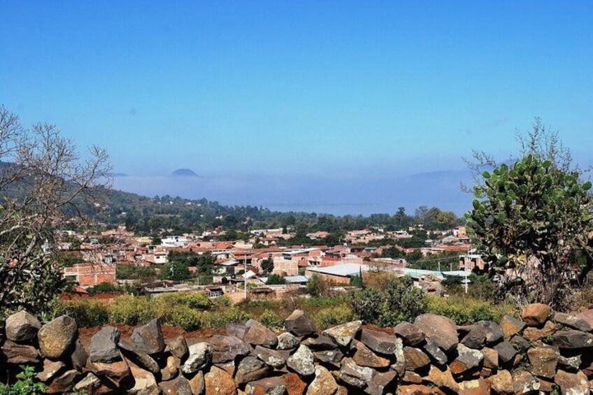A coastal town with red-roofed buildings, a rocky foreground, and a clear blue sky. 4