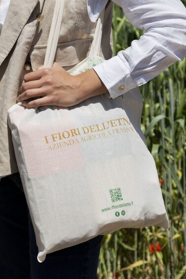 Een persoon draagt een beige tas met goudkleurige letters en een QR-code. 2
