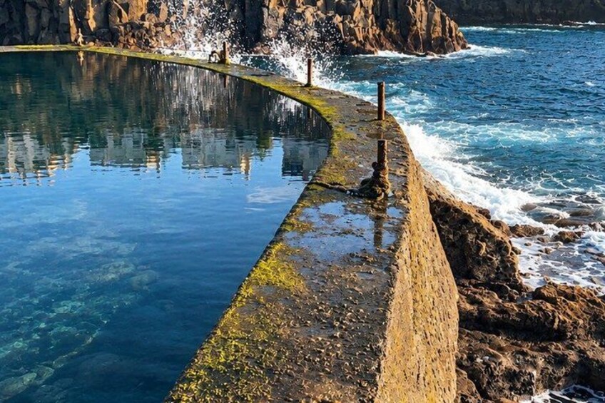 A coastal pool with clear water, surrounded by rocky cliffs and waves crashing onto the shore. 5