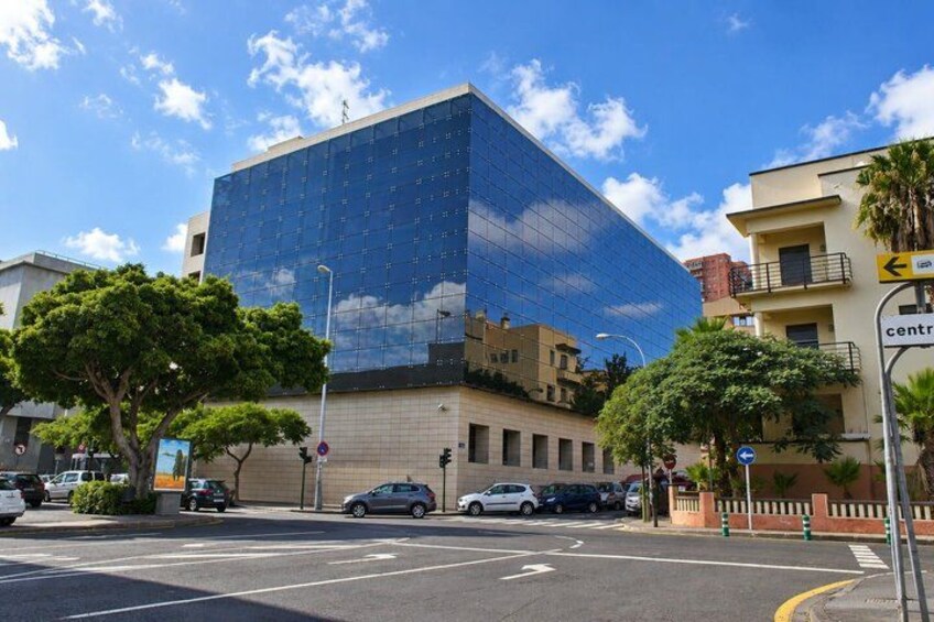 A modern building with a glass facade, a street with cars, and a clear blue sky. 3