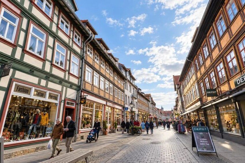 A cobblestone street lined with traditional European buildings, a person walking, and a signboard. 1