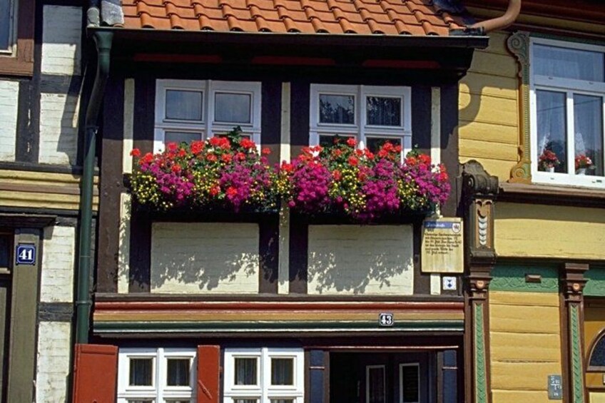 A building with a balcony adorned with colorful flowers, a traditional facade with a tiled roof, and a visible address number. 3