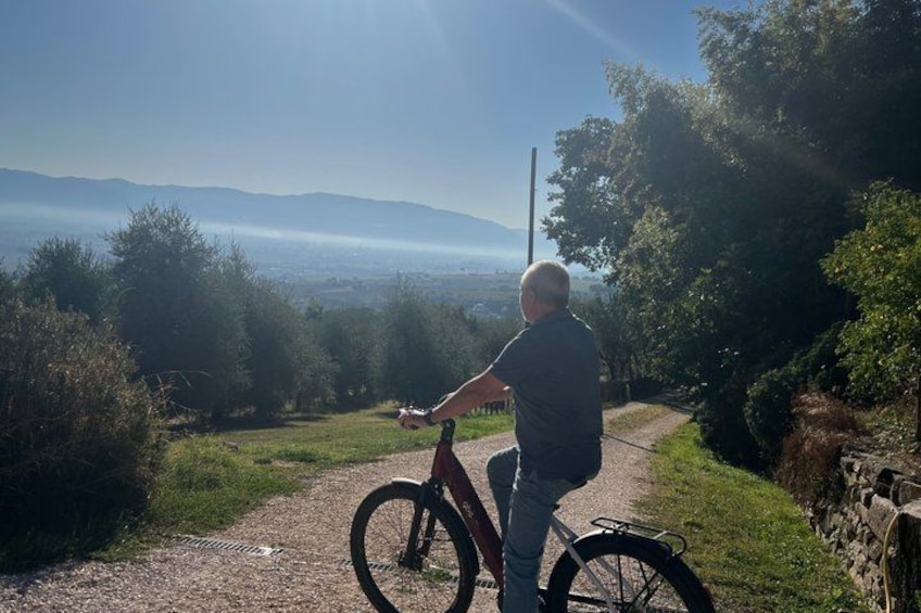 A person standing next to a bicycle on a gravel path with a scenic view of mountains and trees. 1
