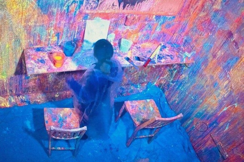 A room with colorful walls and a person painting on a canvas. 2