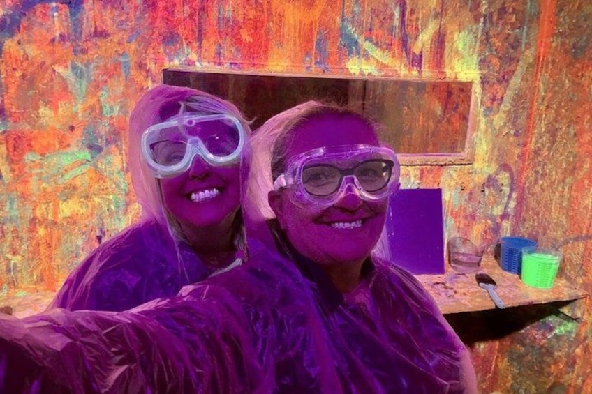 Two people wearing protective gear, likely engaged in a painting activity with a colorful, textured wall in the background. 5