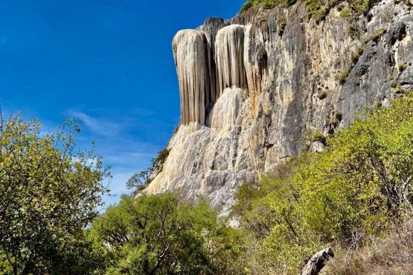 A waterfall cascading down a rocky cliff surrounded by greenery. 1