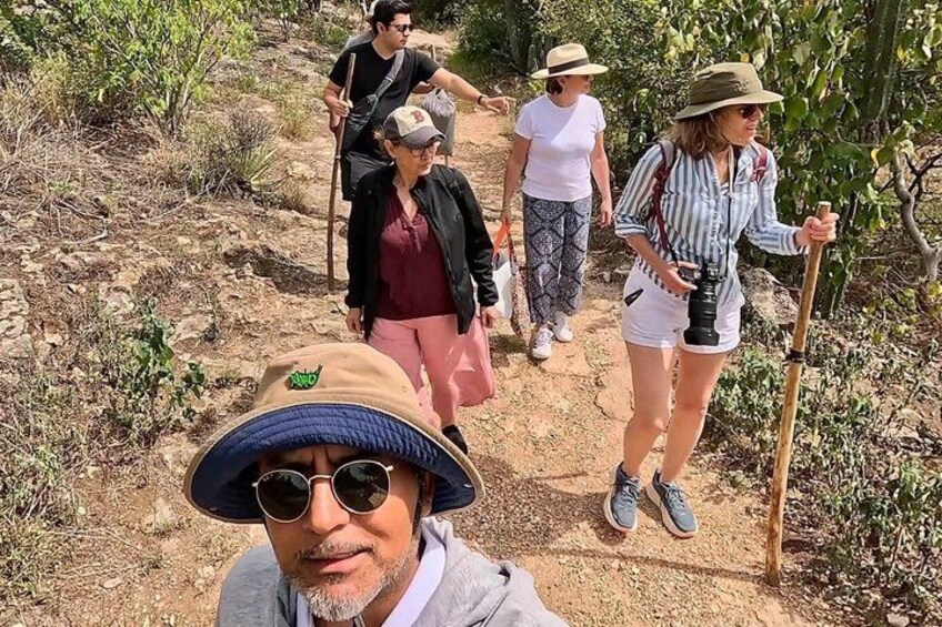 A group of people hiking on a dirt trail surrounded by dry vegetation. 4