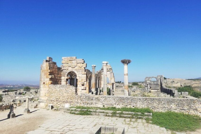 Ancient ruins with stone columns and arches, set against a clear blue sky. 1