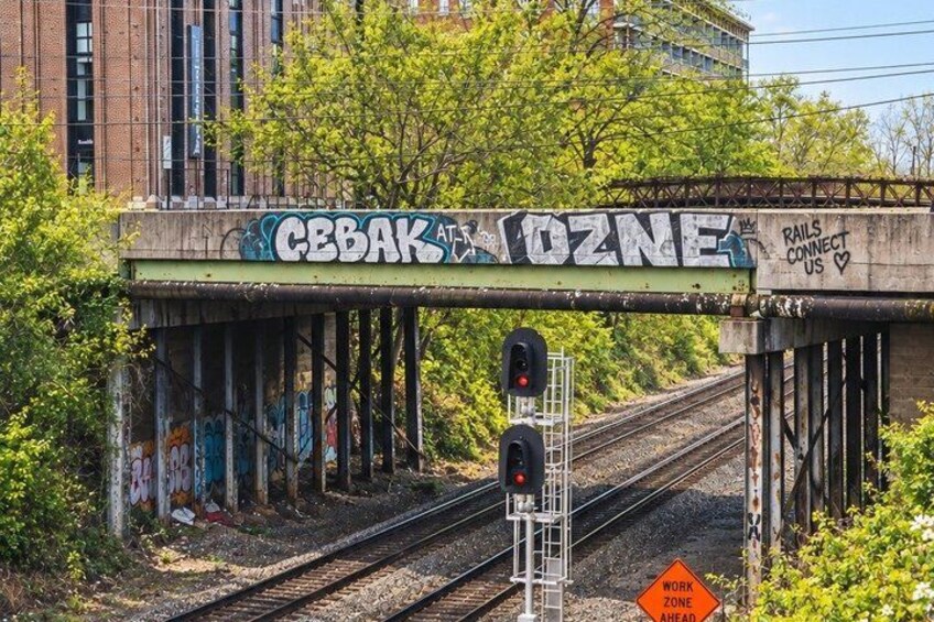 A railway crossing with graffiti on the overhead structure, a red signal light, and a work zone sign. 2