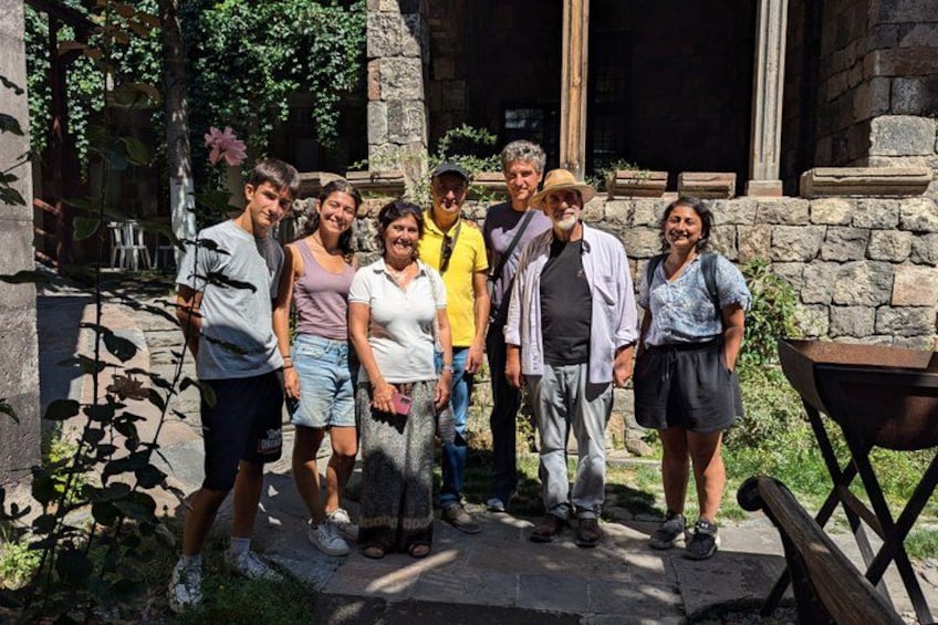 A group of people standing in a garden with stone walls and a wooden structure. 3