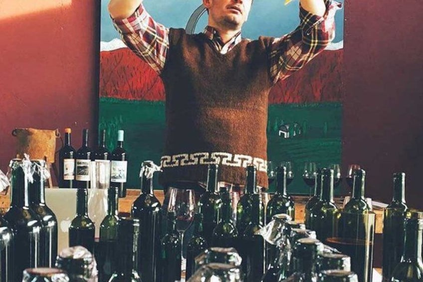 A person standing in front of a wall with a flag, surrounded by numerous bottles of wine. 3