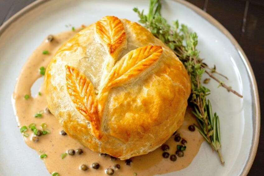 A pastry with leaf-shaped cutouts on top, garnished with herbs and capers, on a plate. 1