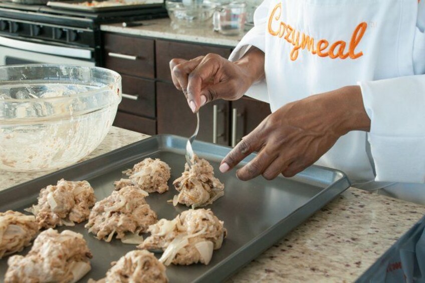 A person preparing food, wearing a white shirt with 'Cozymmeal' on it, in a kitchen with a stove and a countertop. 4