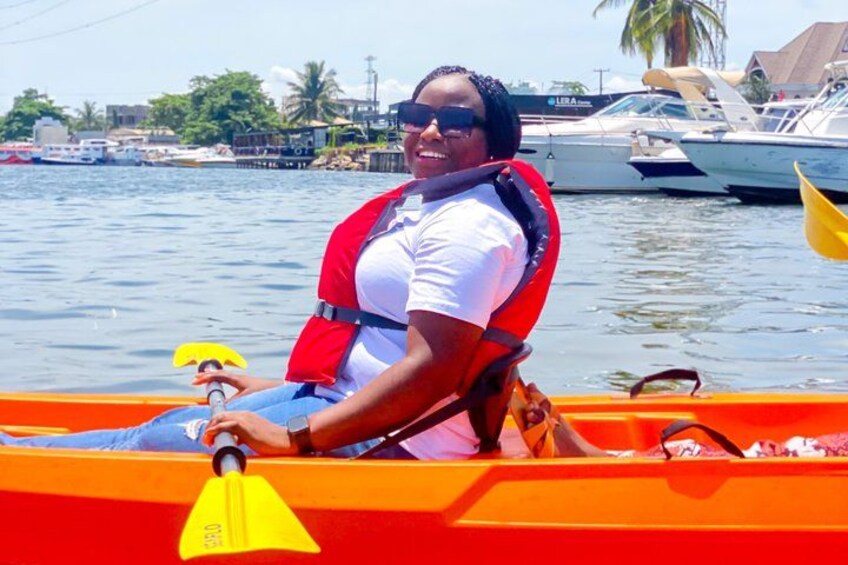 A person in a canoe on a body of water with boats in the background. 1