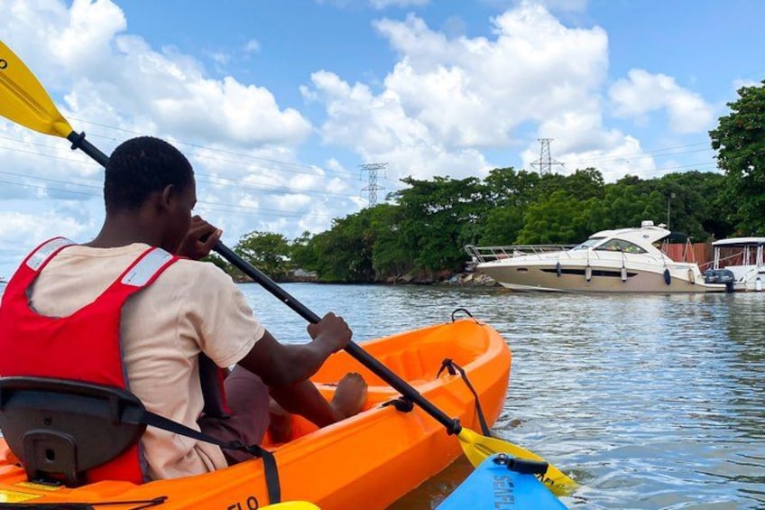A person in a kayak on a calm body of water, with a boat docked in the background and trees lining the shore. 3