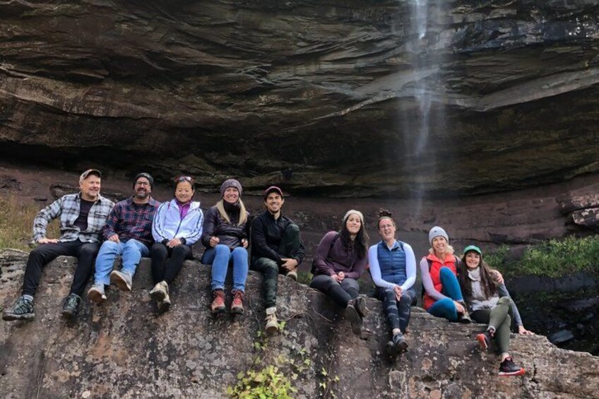 A group of people sitting on a rock formation with a waterfall in the background. 1