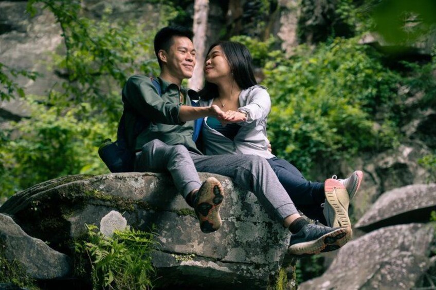 Two people sitting on a rock with greenery in the background. 2