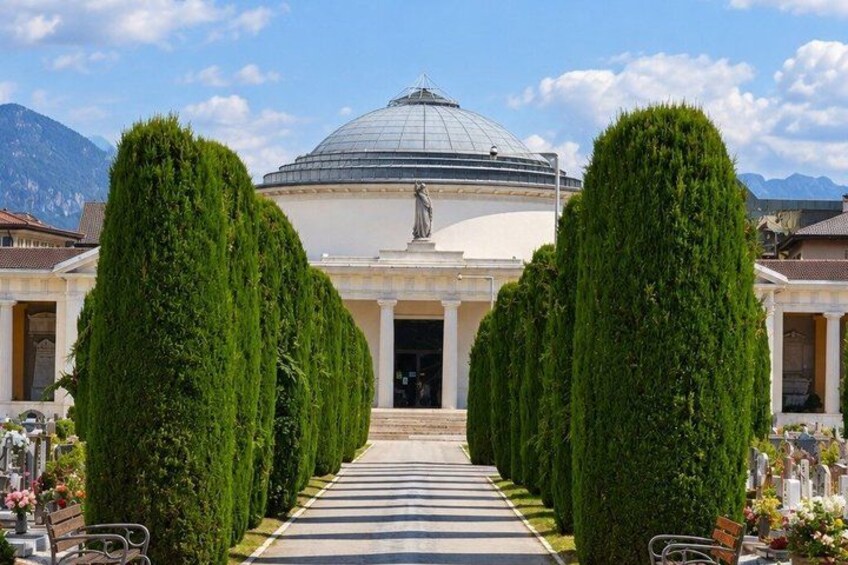 A building with a dome and a statue in front, flanked by tall, green trees. 4