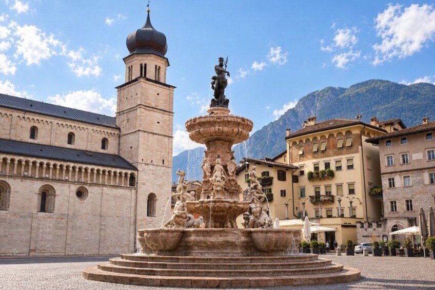 A historic fountain with statues, a church with a bell tower, and buildings with balconies. 1