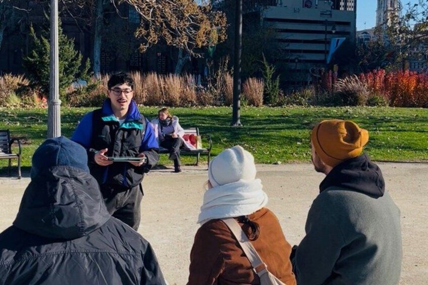 A group of people in a park, some holding tablets, with benches and trees in the background. 4