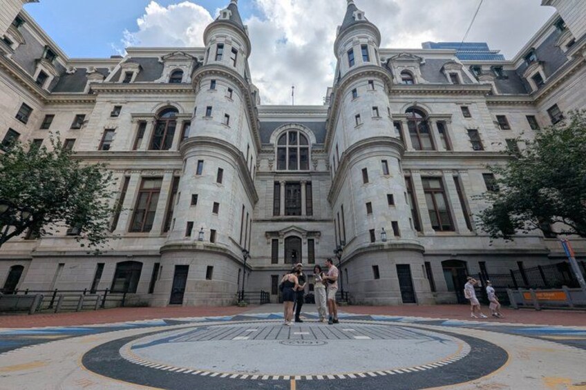 A historic building with classical architecture, a circular plaza with a patterned design, and a clear sky. 1