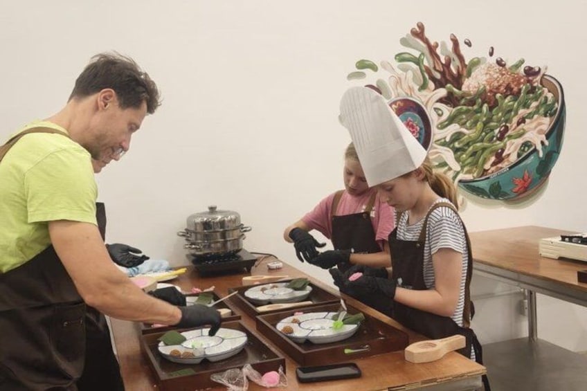 A person preparing food, another person wearing a chef's hat, and a painting on the wall. 5