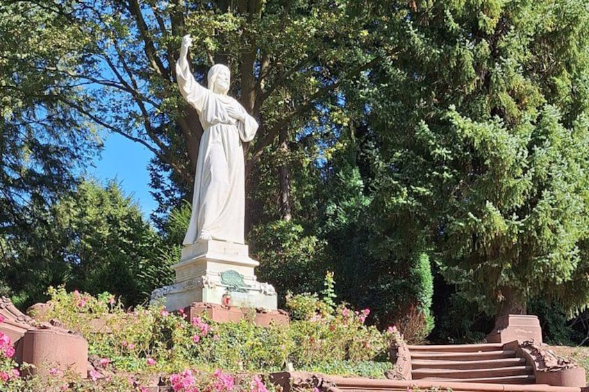 A statue of a woman in a flowing robe, surrounded by lush greenery and a stone staircase. 1