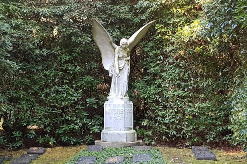A statue of an angel with outstretched wings, set on a pedestal with inscriptions, surrounded by lush greenery. 4