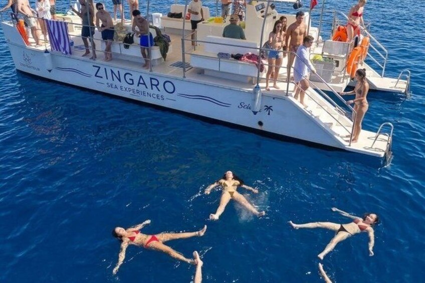 A boat named ZINGARO with people swimming and standing on it. 2