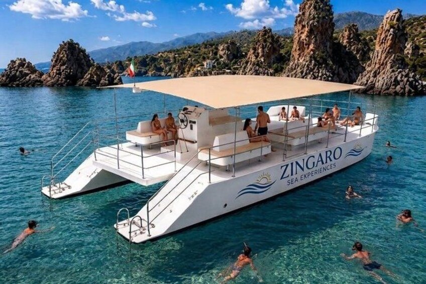 A white boat named ZINGARO with people on board and swimmers in the water. 1