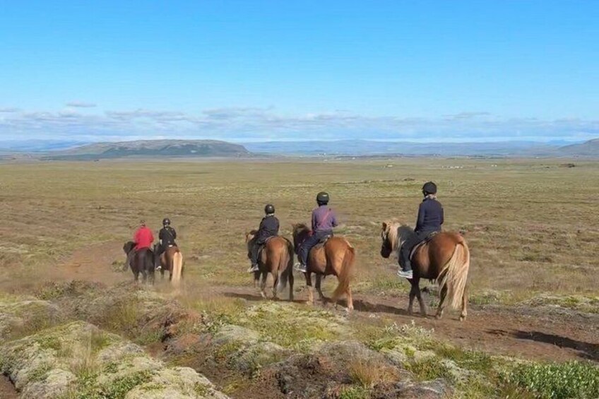 A group of people riding horses across a grassy field with distant mountains. 1