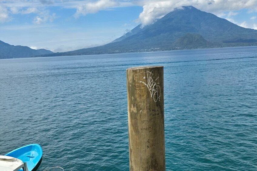 A wooden post with graffiti, a blue boat, and a mountain in the background. 2
