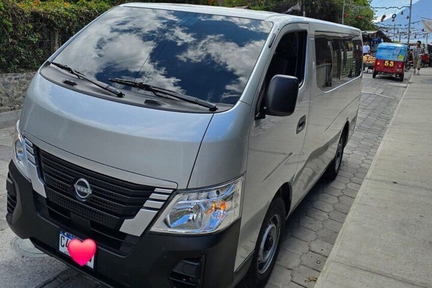 A silver van parked on a sidewalk with a license plate and a heart sticker. 5