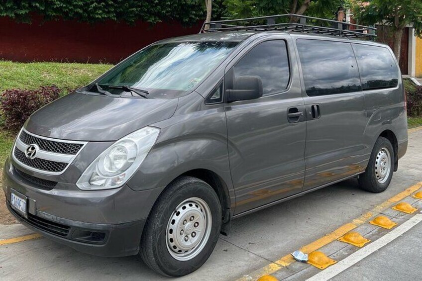 A gray minivan parked on a street with yellow road markings. 1