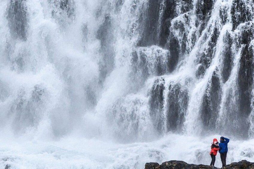 A waterfall with two people observing it. 2