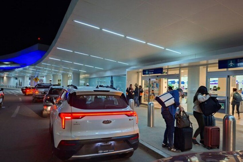 A white SUV parked at a terminal with passengers and luggage. 5