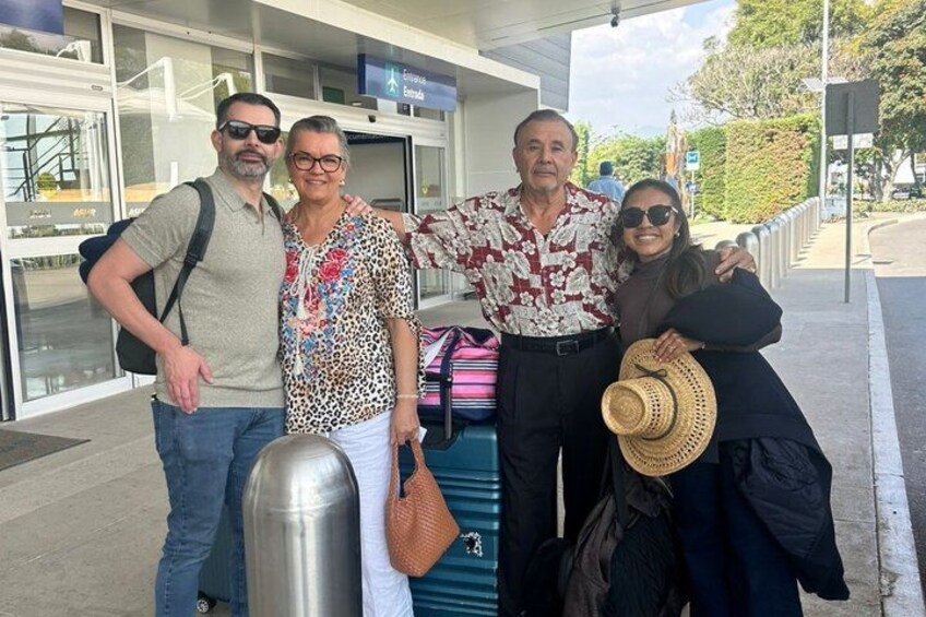A group of people at an airport with luggage and a building in the background. 1