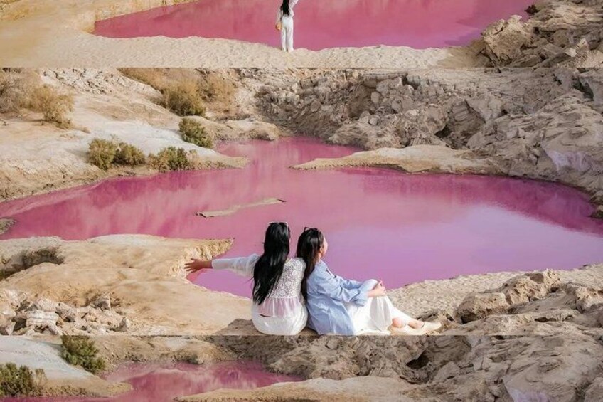 Two people sitting on rocks by a pink mineral pool. 1